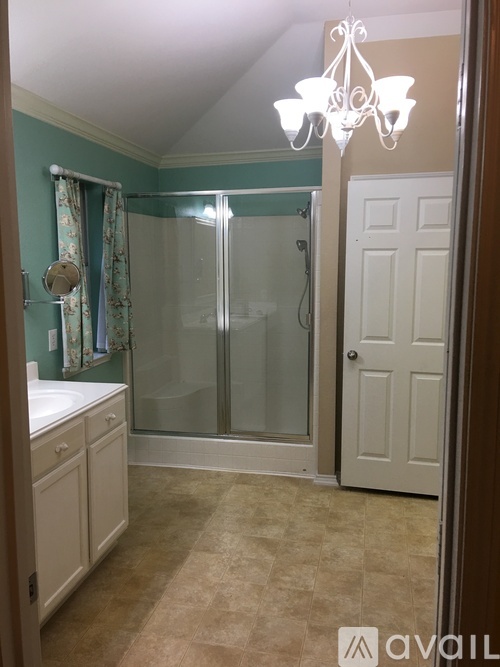 A bathroom with a white door, a chandelier, and a shower with a glass door.