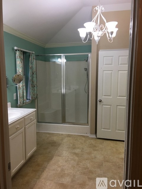 A bathroom with a white door, a chandelier, and a shower with a glass door.