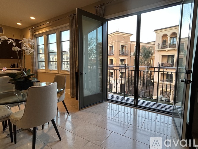 A dining room with a glass table and chairs with a view of a balcony outside.