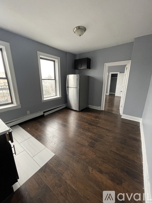 A kitchen with a refrigerator, a window, and a door leading to another room.