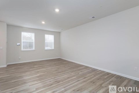 A room with wooden flooring and two windows.