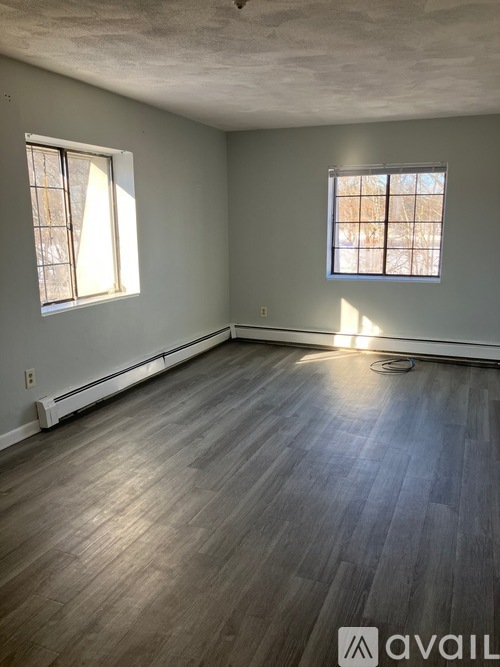 A room with wooden flooring and two windows.