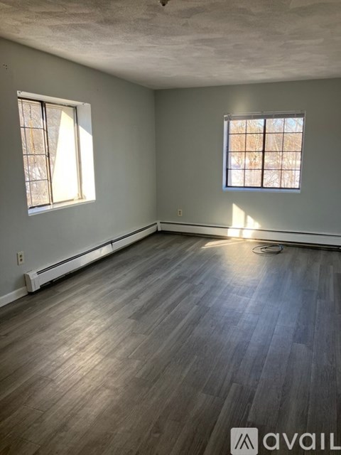 A room with wooden flooring and two windows.