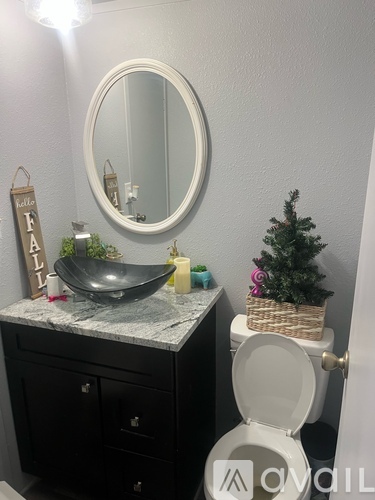 A bathroom with a toilet, sink, mirror, and a small Christmas tree.