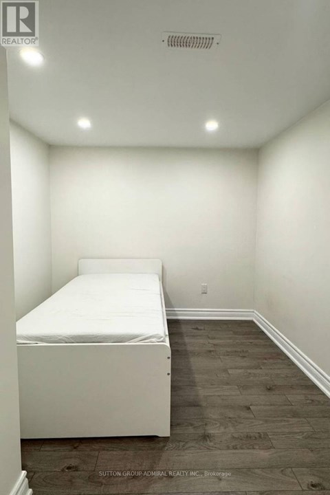 A bedroom with a white bed and wooden flooring.