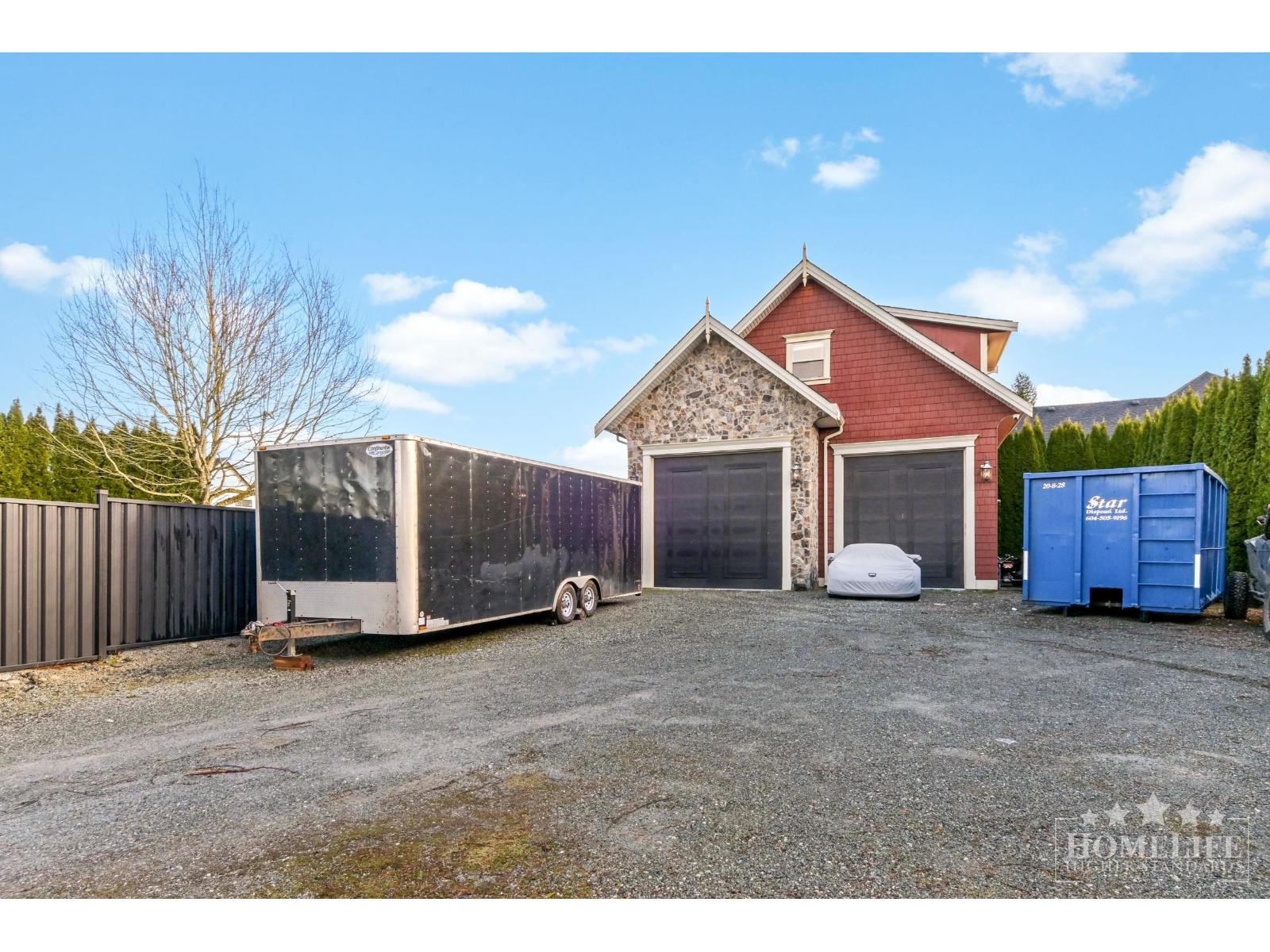 A gravel lot with a trailer, a red building, and a blue dumpster.