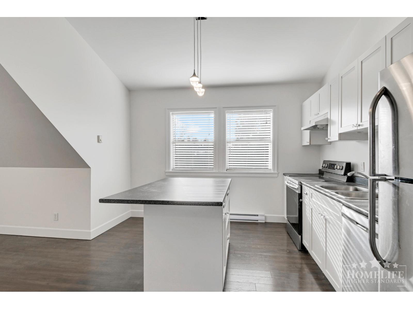 A kitchen with a stainless steel refrigerator and a window with blinds.