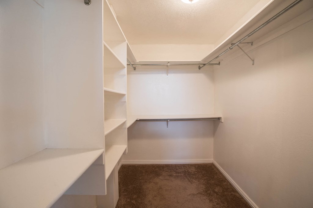 a walk in closet with shelves and a white wall