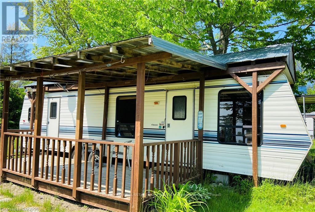 A white RV with a wooden deck is parked in a grassy area.