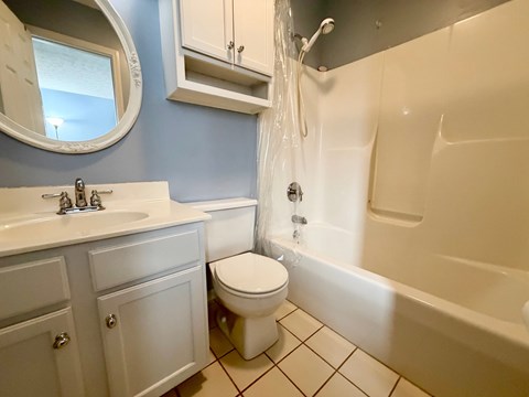 A white toilet sits in a bathroom next to a sink and bathtub.