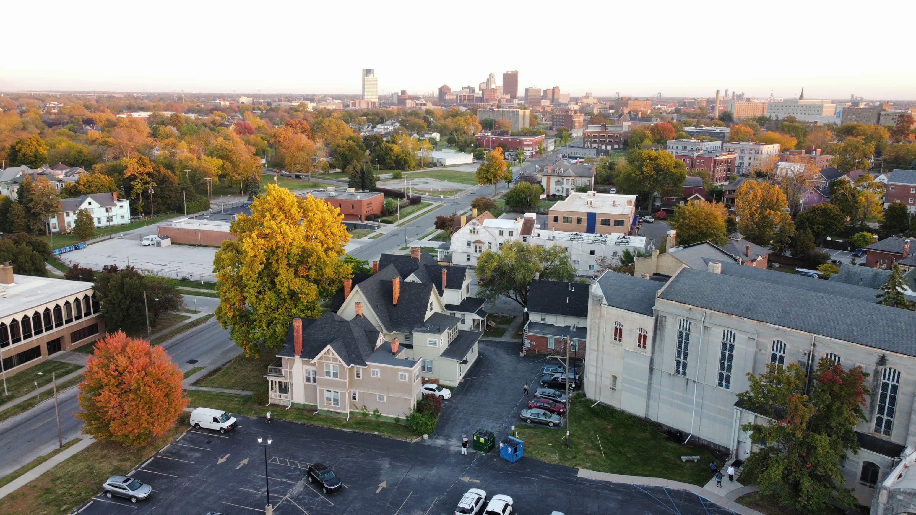 A parking lot is in the foreground of a town with a large building in the middle.