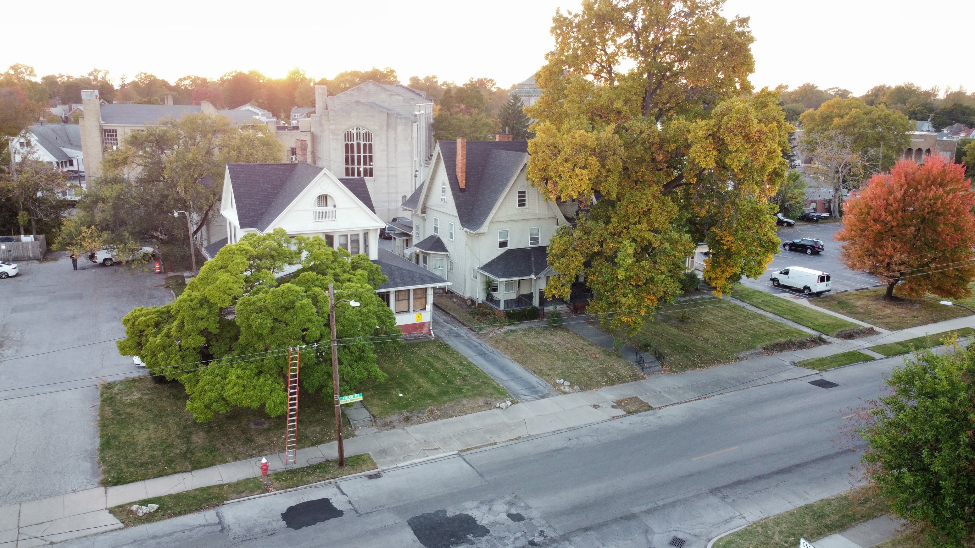 A house with a white facade and a grey roof is surrounded by trees with green, yellow and red leaves.