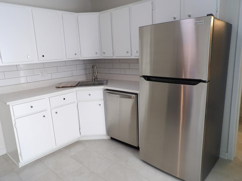A stainless steel refrigerator stands in a kitchen with white cabinets.