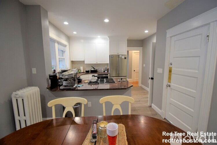 A kitchen with a table and chairs in the foreground and a hallway in the background.