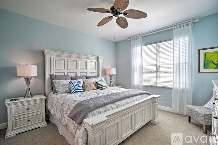 A bedroom with a large bed, a ceiling fan, and a window with blinds.