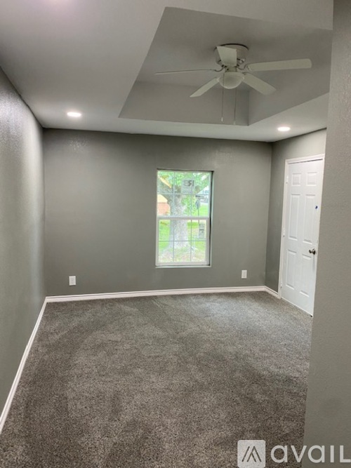 A room with a ceiling fan and a window with a view of trees and a house.