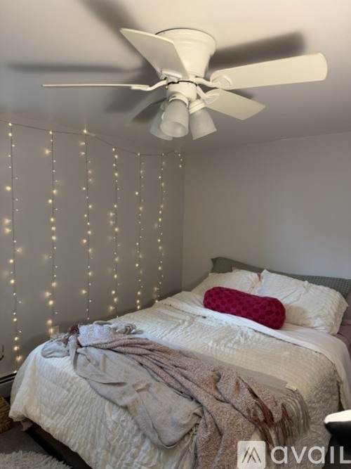A bedroom with a bed, a ceiling fan, and a wall covered in string lights.