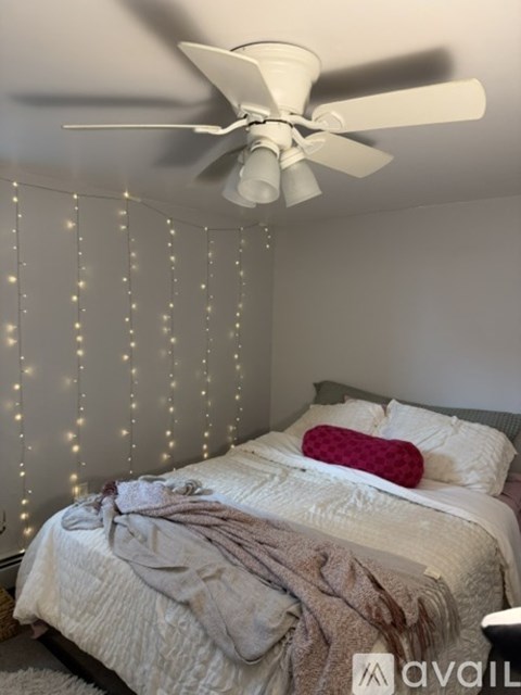 A bedroom with a bed, a ceiling fan, and a wall covered in string lights.