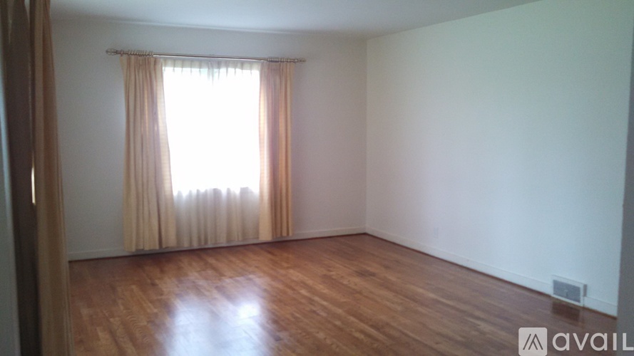 A room with wooden flooring and a window with curtains.