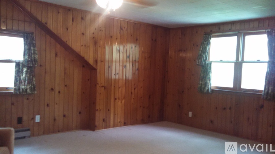 A room with wooden walls and a window with a green curtain.