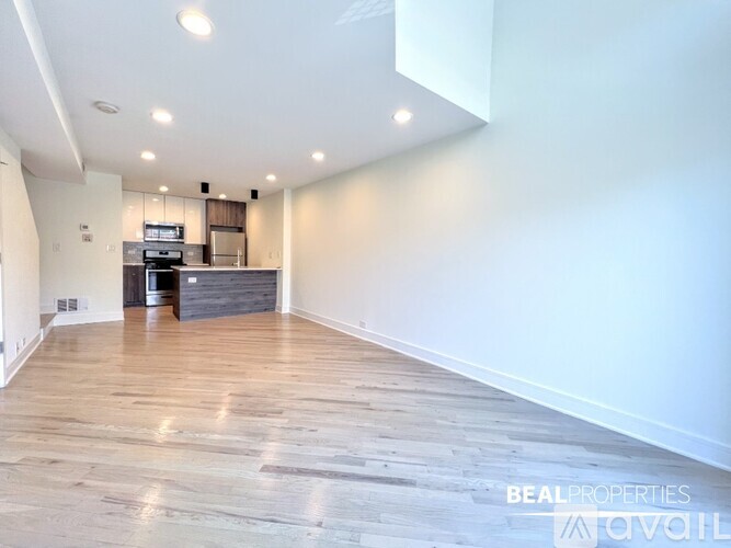 A spacious room with wooden flooring and a kitchen area in the background.