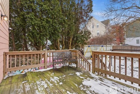 A deck with a wooden railing and a bench is surrounded by trees.
