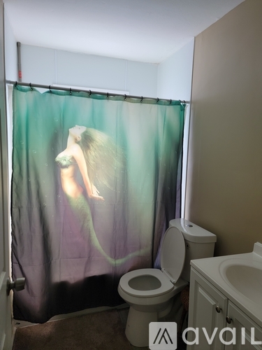 A bathroom with a toilet, sink and a shower curtain with a mermaid on it.