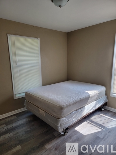 A bedroom with a bed covered in a white sheet and a window with blinds.