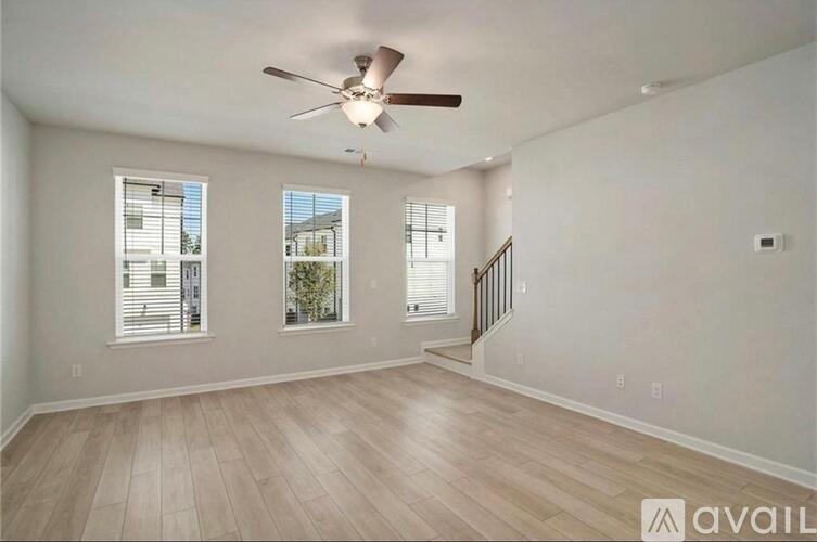 A spacious room with a ceiling fan and light, hardwood flooring, and three windows.