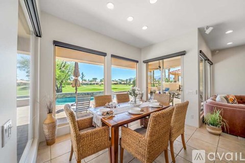 A dining room with a table set for six with a view of a pool and trees outside.