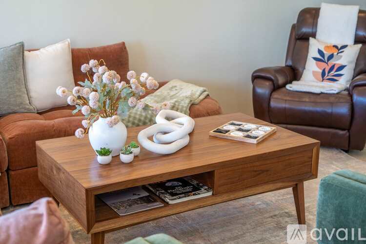 A living room with a brown couch, a coffee table with a vase of flowers, a magazine, and a white sculpture.