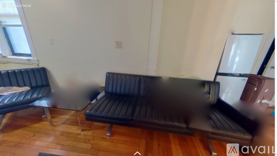 A black couch with a wooden floor and a window in the background.
