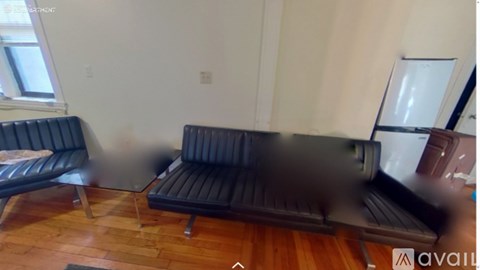 A black couch with a wooden floor and a window in the background.