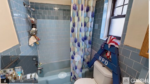 A bathroom with a blue tiled shower and a toilet with a flag on it.