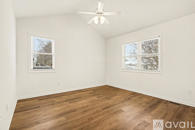 A room with wooden flooring and two windows with blinds.