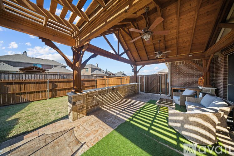 A wooden pergola over a patio with a stone wall and grass.