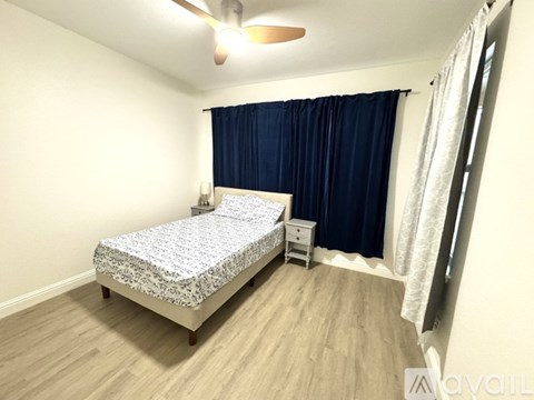 A bedroom with a patterned bedspread, a ceiling fan, and a nightstand with a lamp.