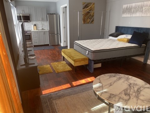 A bedroom with a bed, a table, and a kitchen area.
