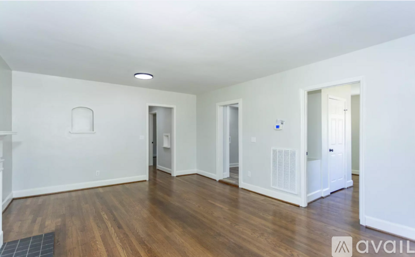 A spacious room with wooden floors and white walls, featuring a central doorway and two side doorways.