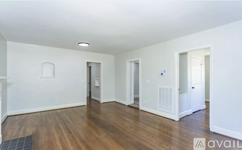A spacious room with wooden floors and white walls, featuring a central doorway and two side doorways.