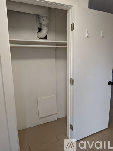 A white closet with a door and a white pipe sticking out of the top shelf.
