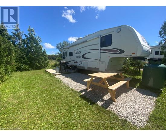 A white RV is parked in a grassy area with a picnic table in front of it.