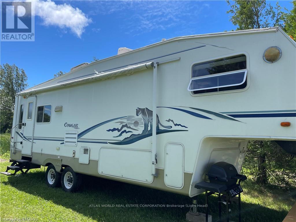 A white RV with a blue stripe and a fish design is parked on grass.