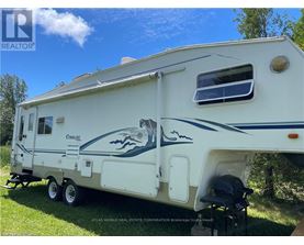A white RV with a blue stripe and a fish design is parked on grass.