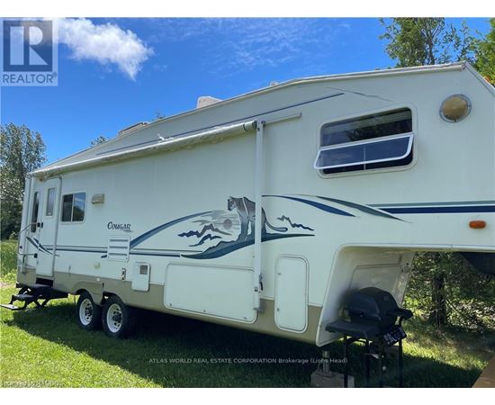 A white RV with a blue stripe and a fish design is parked on grass.