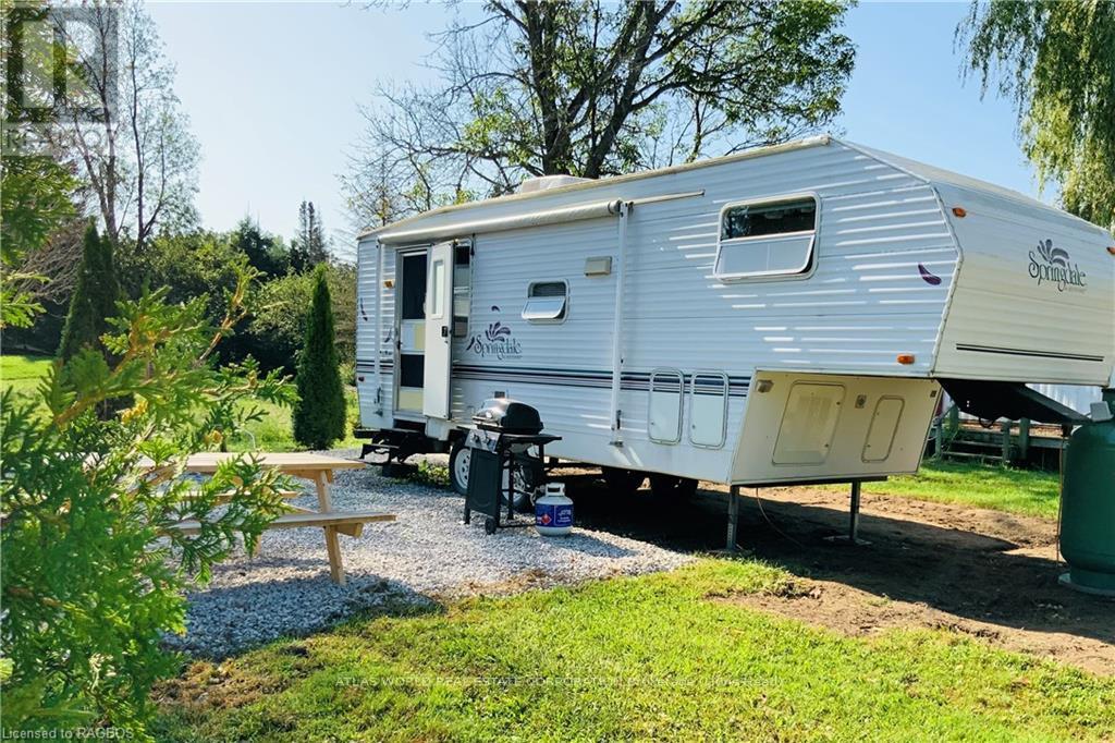 A silver caravan is parked in a grassy area with a picnic table and a tree nearby.