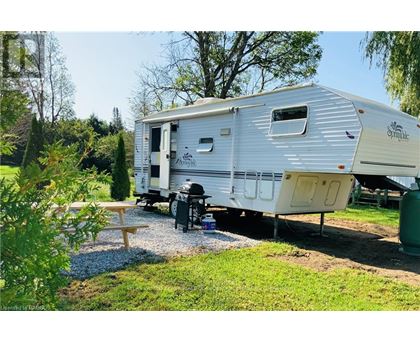 A silver caravan is parked in a grassy area with a picnic table and a tree nearby.