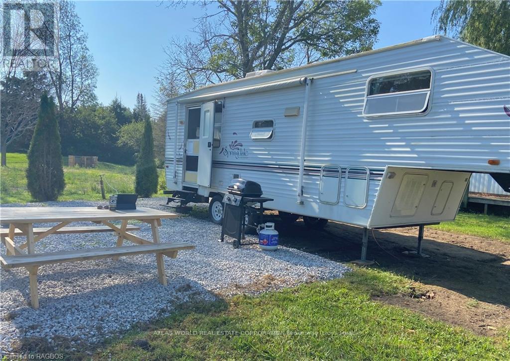 A silver trailer is parked in a gravel lot with a picnic table in front of it.