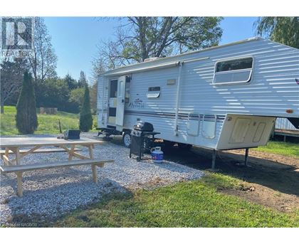 A silver trailer is parked in a gravel lot with a picnic table in front of it.