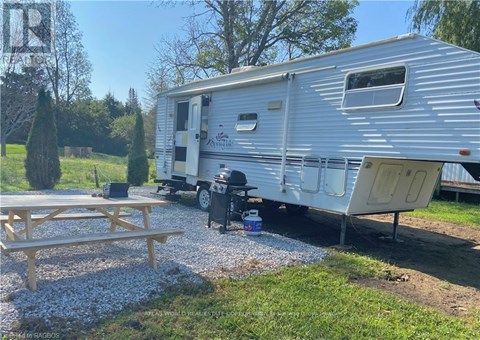 A silver trailer is parked in a gravel lot with a picnic table in front of it.